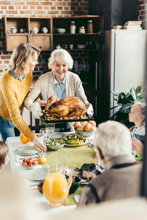 senior woman and her daughter carrying turkey for thanksgiving dinner with their beautiful familyの写真素材