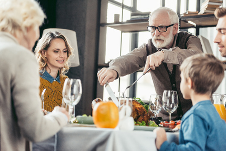 grandfather cutting turkey for family on thanksgiving holiday dinnerの写真素材