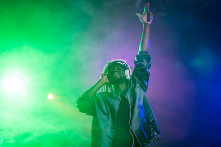 professional african american club DJ in headphones in nightclub with back lightの写真素材