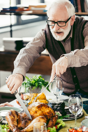happy senior man cutting delicious turkey on holiday dinnerの写真素材