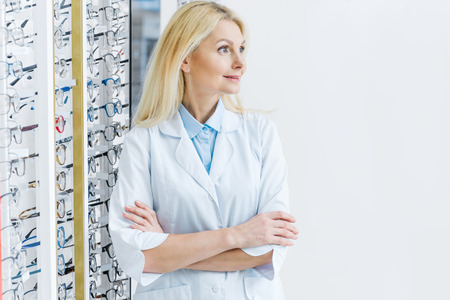 female ophthalmologist standing in optics with glasses on shelvesの写真素材