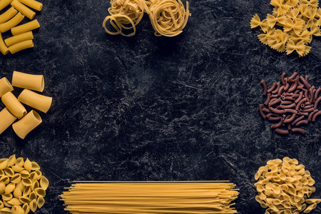 top view composition of various raw pasta on black concrete tableの写真素材