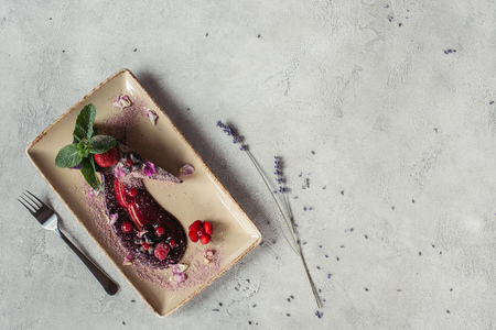 food composition with piece of blueberry cake served with mint leaves and violet petals on plate on grey tabletopの写真素材