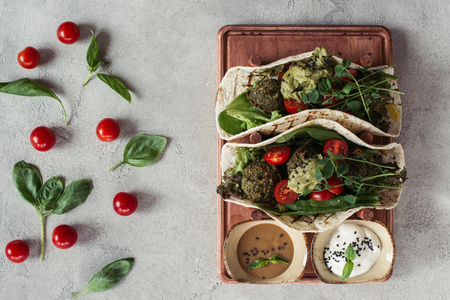 flat lay with falafel with tortillas, cherry tomatoes and germinated seeds of sunflower served on wooden board on grey surfaceの写真素材