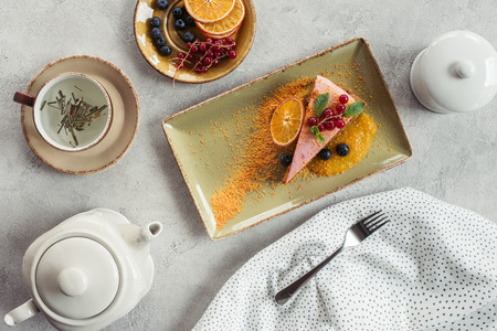 flat lay with piece of sweet carrot cake with berry filling, teapot and cup of herbal tea on grey tabletopの写真素材