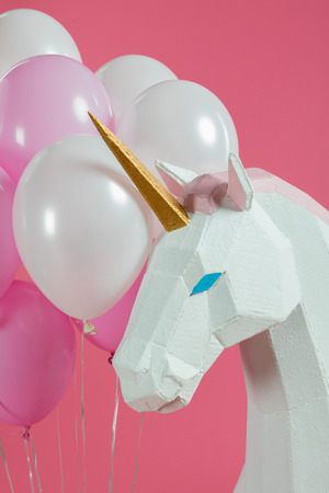Head of decorative unicorn by bunch of balloons isolated on pinkの写真素材