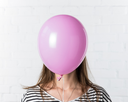 Pink balloon covering face of young woman on white brick wall backgroundの写真素材
