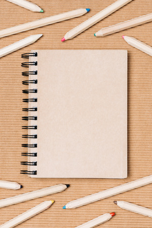 flat lay with arrangement of empty notebook and colorful pencils on brown backdropの写真素材