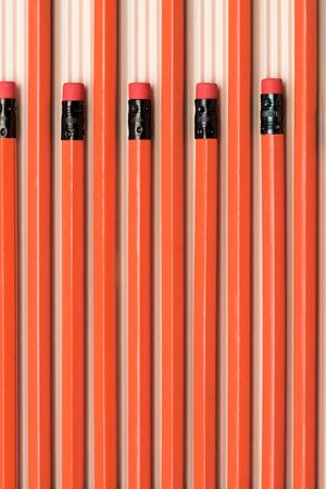 top view of red graphite pencils with erasers placed in row on beigeの写真素材
