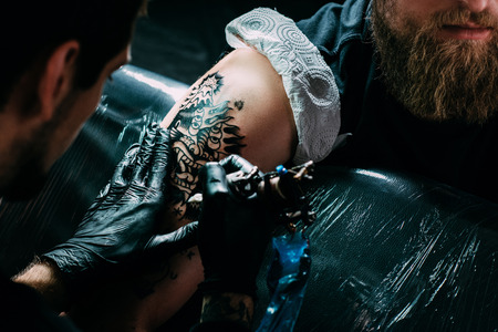 cropped shot of tattoo artist in gloves working on tattoo on shoulder in salonの写真素材
