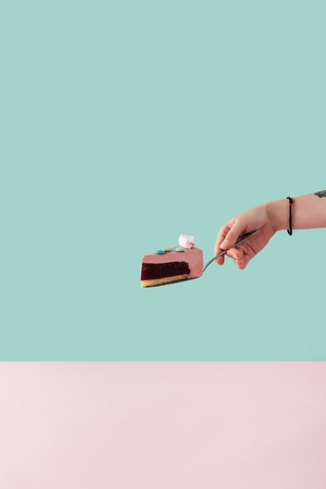 cropped view of tattooed hand with piece of cake with marshmallow on cake shovel