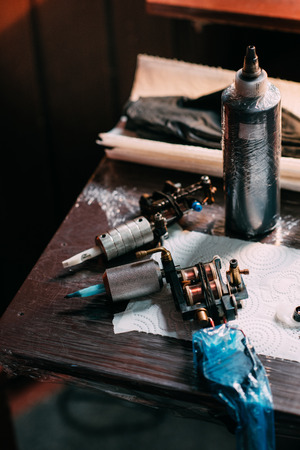 close up view of tattoo machines and paint on wooden tabletop at tattoo salonの写真素材
