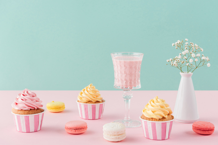 cupcakes and sweet macarons and glass of milkshake on pastel backgroundの写真素材