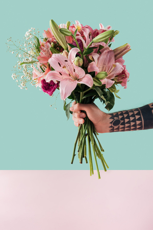 cropped view of tattooed male hand with bouquet of pink lily flowersの写真素材
