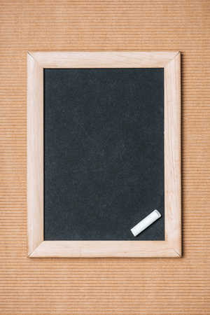 top view of empty blackboard and piece of chalk on brown backgroundの写真素材