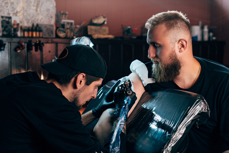 side view of tattoo artist in gloves working on tattoo on shoulder in salonの写真素材