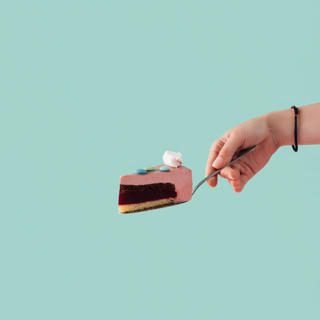 cropped view of tattooed hand with piece of cake on cake shovel isolated on blue