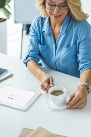 smiling blonde businesswoman with cup of coffee using tablet with Google websiteのeditorial素材