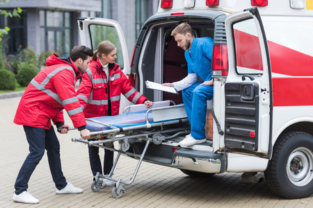young paramedics moving out ambulance stretcher from carの写真素材