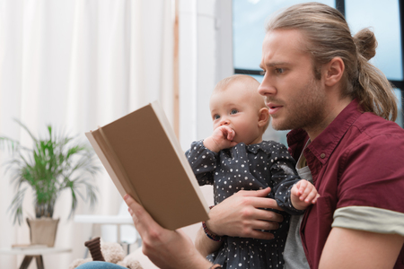 father reading book to little daughter at homeの写真素材