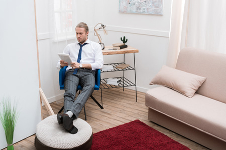 Businessman sitting on chair at home and using tabletの写真素材