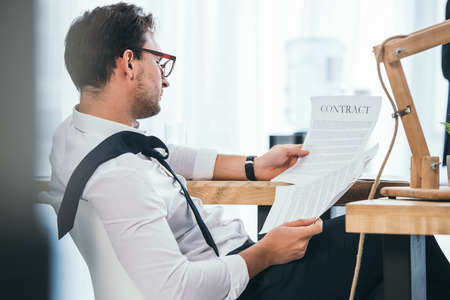 untidy overworked businessman discovering contract at workplaceの写真素材