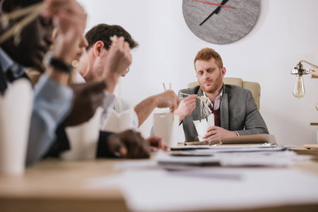 group of businesspeople eating noodles together at office with boss