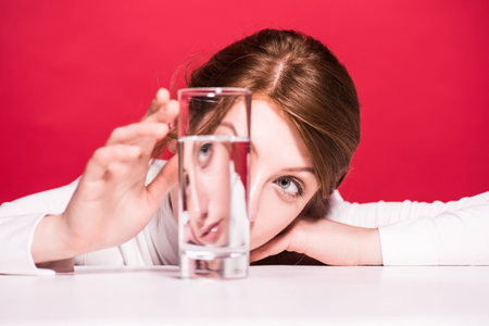 close-up view of upset young woman looking at glass of water isolated on red
