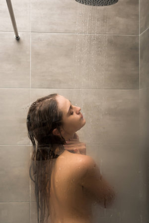 View through steamy shower glass cabin on a woman washing bodyの写真素材
