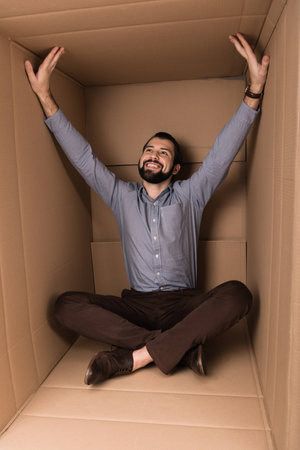 cheerful man sitting in cardboard box, introvert concept
