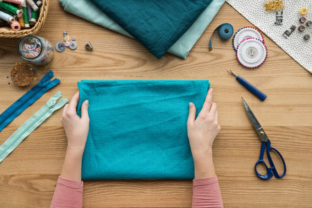 top view of cropped female hands folding fabric at seamstress workplace