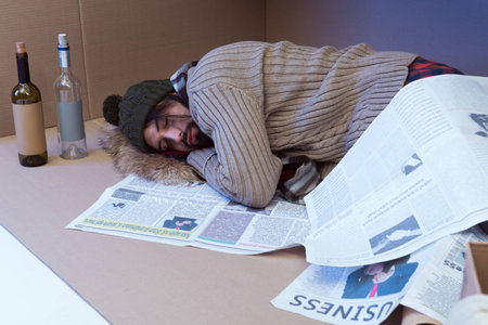 homeless man with bottles sleeping in cardboard box
