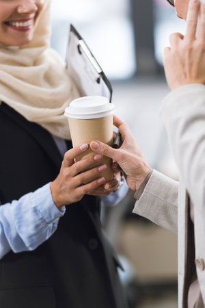 partial view of smiling businesswoman giving coffee to colleague at work in officeの写真素材