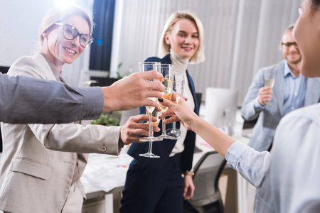 partial view of business colleagues clinking glasses of champagne during celebration in office