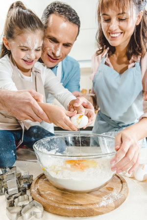 cropped image of happy family splitting egg in bowl at kitchen