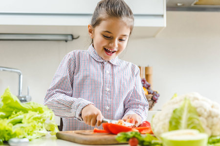 happy kid slicing pepper on chopping board at kitchenの写真素材