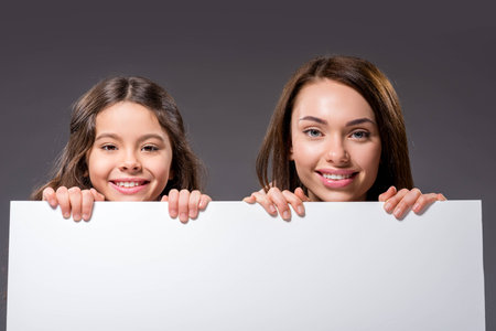 Mother and daughter holding empty white board isolated on grayの写真素材