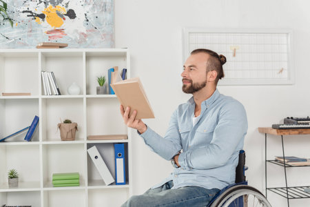 happy disabled man on wheelchair reading book with thoughtful lookの写真素材
