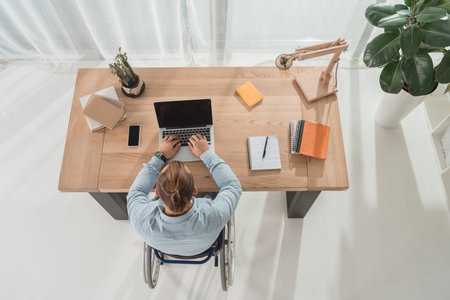top view of disabled man on wheelchair using laptop at office