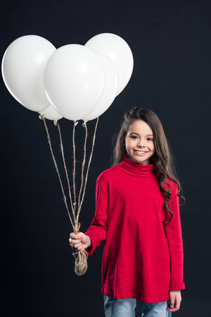 Smiling kid holding bundle of white balloons isolated on blackの写真素材