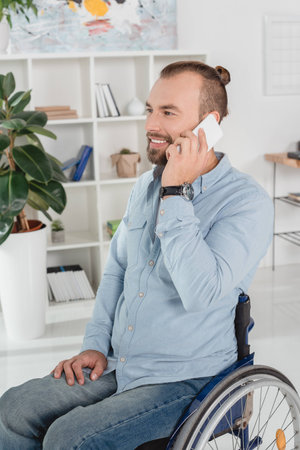 smiling disabled man on wheelchair talking by phone