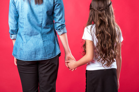 Cropped image of mother and daughter standing and holding hands isolated on redの写真素材
