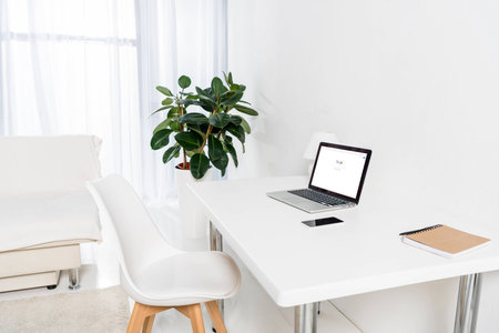 laptop with google logo, smartphone and notebook on table in living roomのeditorial素材