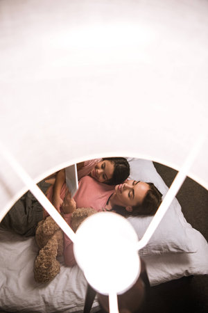 overhead view of mother and daughter using tablet together while lying on bed at homeの写真素材