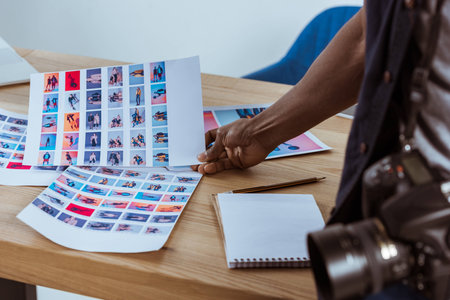 partial view of african american photographer holding photoshoot examples at workplace in officeの写真素材