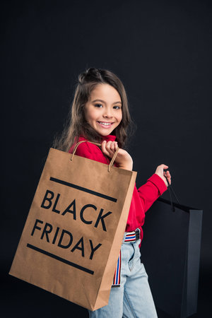 Smiling kid holding shopping bag on black friday isolated on blackの写真素材