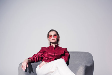 attractive stylish girl posing on armchair for fashion shoot, isolated on greyの写真素材