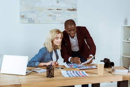 portrait of multiethnic photographers looking at portfolio at workplace in officeの写真素材