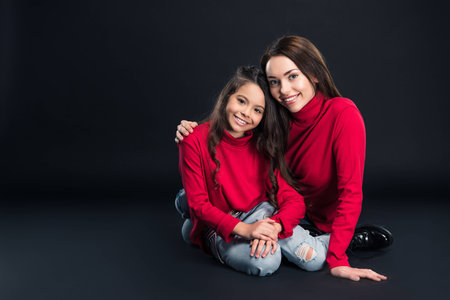Mother sitting and hugging daughter isolated on blackの写真素材