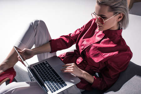 attractive stylish girl in red sunglasses using laptop, on greyの写真素材
